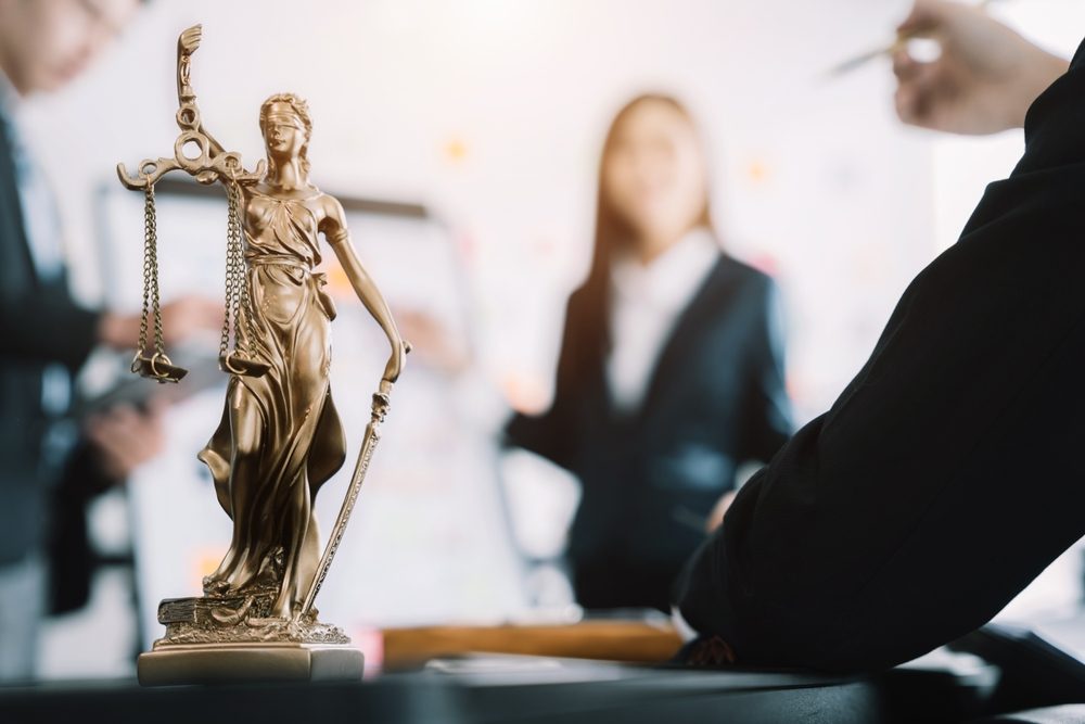statue of justice with scales and auction hammer, the team meeting at the law firm behind the concept of in office law.